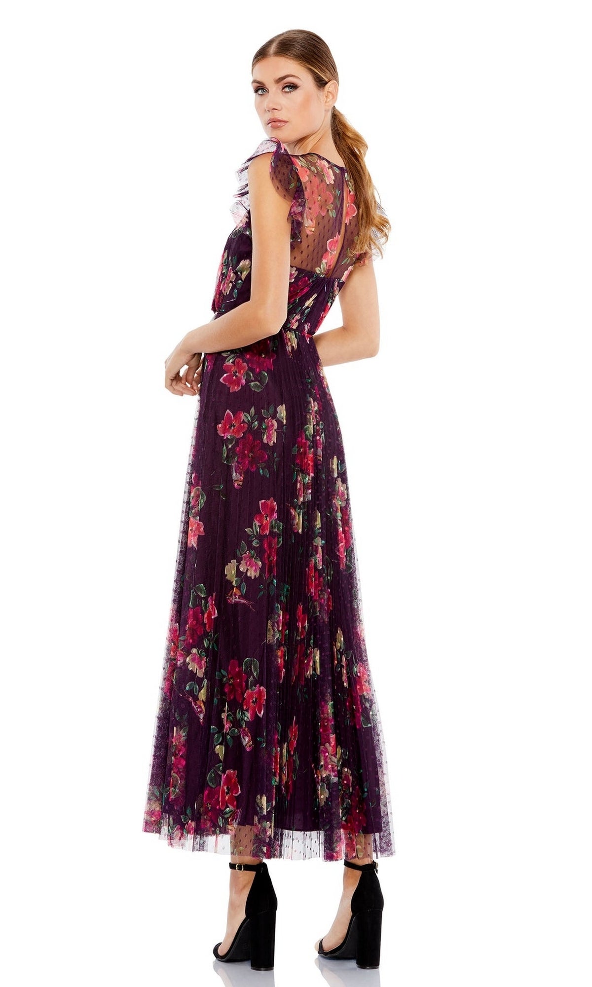 A woman models the Plum Print Midi Semi-Formal Dress: Mac Duggal 2143, featuring a floral pattern and sheer back detailing, paired with black block-heeled shoes as she stands looking over her shoulder.